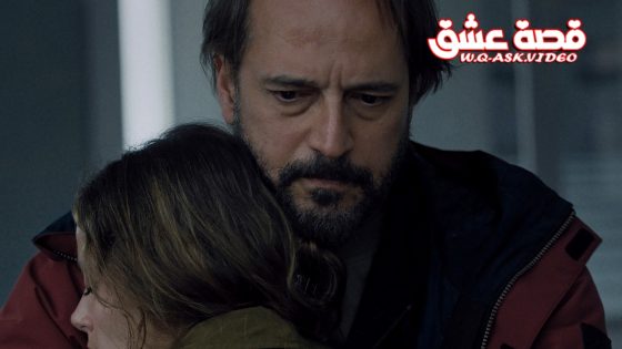 Man with a beard comforts a woman by embracing her head on his shoulder.